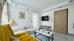 Ein modernes Wohnzimmer mit einem gelben Sofa, einem Marmortisch, einem an der Wand befestigten Fernseher und einer Holztür.