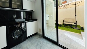 Eine moderne Küche mit integrierter Waschmaschine und Trockner, eine Glastür führt zu einer Terrasse mit Bank und Sonnenschirm.