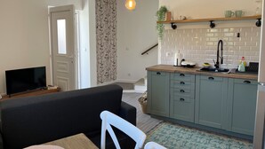 A compact living space with a kitchenette, a dining area with a table and chairs, a television, and a staircase leading to another level. - Casa da Calabra by Trip2Portugal (Vila Nova de Foz Coa)