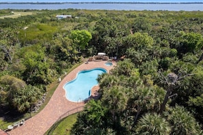 A large swimming pool surrounded by lush greenery, with a view of the ocean in the background.