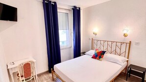 A bedroom with a bed, a desk, a chair, a TV, and a window with curtains. - Hotel Appia (Cannes)