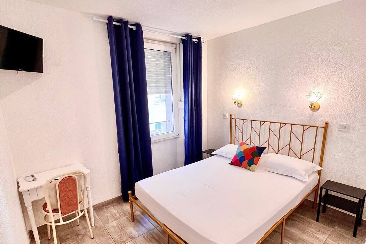 Een slaapkamer met een bed, een bureau, een stoel, een televisie en een raam met gordijnen.