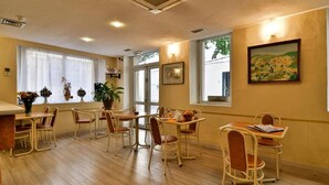 A dining area with multiple tables and chairs, a potted plant, and a painting on the wall. - Hotel Appia (Cannes)