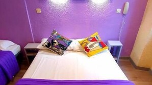 A room with two beds, each with purple bedding, a white headboard, and a small bedside table with a lamp. - Hotel Appia (Cannes)