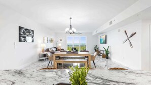 A modern living room with a dining area, a chandelier, and a large window.