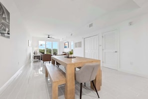 A modern dining area with a wooden table, benches, and chairs. There are windows with a view of greenery.