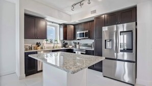 A modern kitchen with dark cabinets, stainless steel appliances, and a central island. - RIVER FLY IN: The Cocoa, Island Horizon View (Merritt Island)