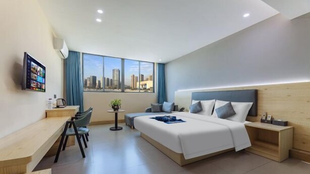A modern hotel room with a large bed, a desk, a chair, a small table with a plant, and a city view. - Heyi Express Hotel (Zhuhai Baijiao Science Park Doumen Bus Terminal) (Zhuhai)