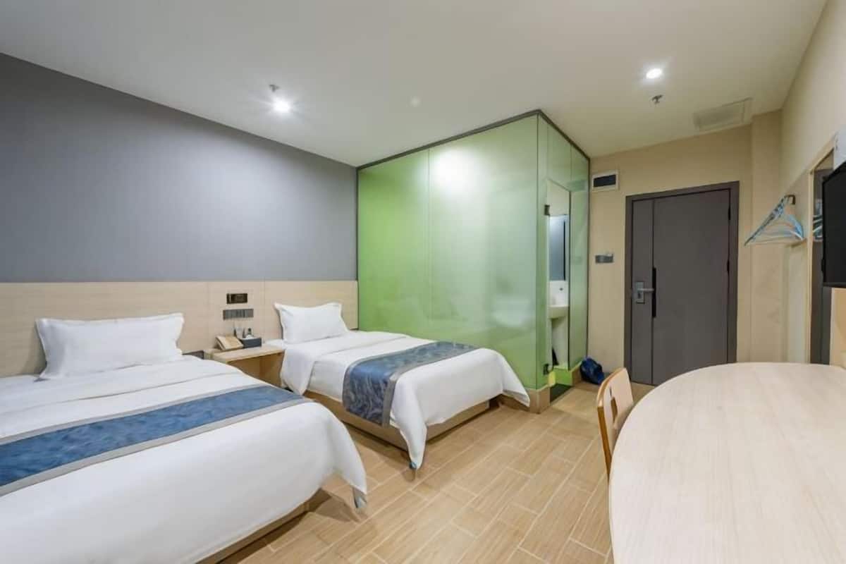 A hotel room with two beds, a green partition wall, a round table, and a TV mounted on the wall.