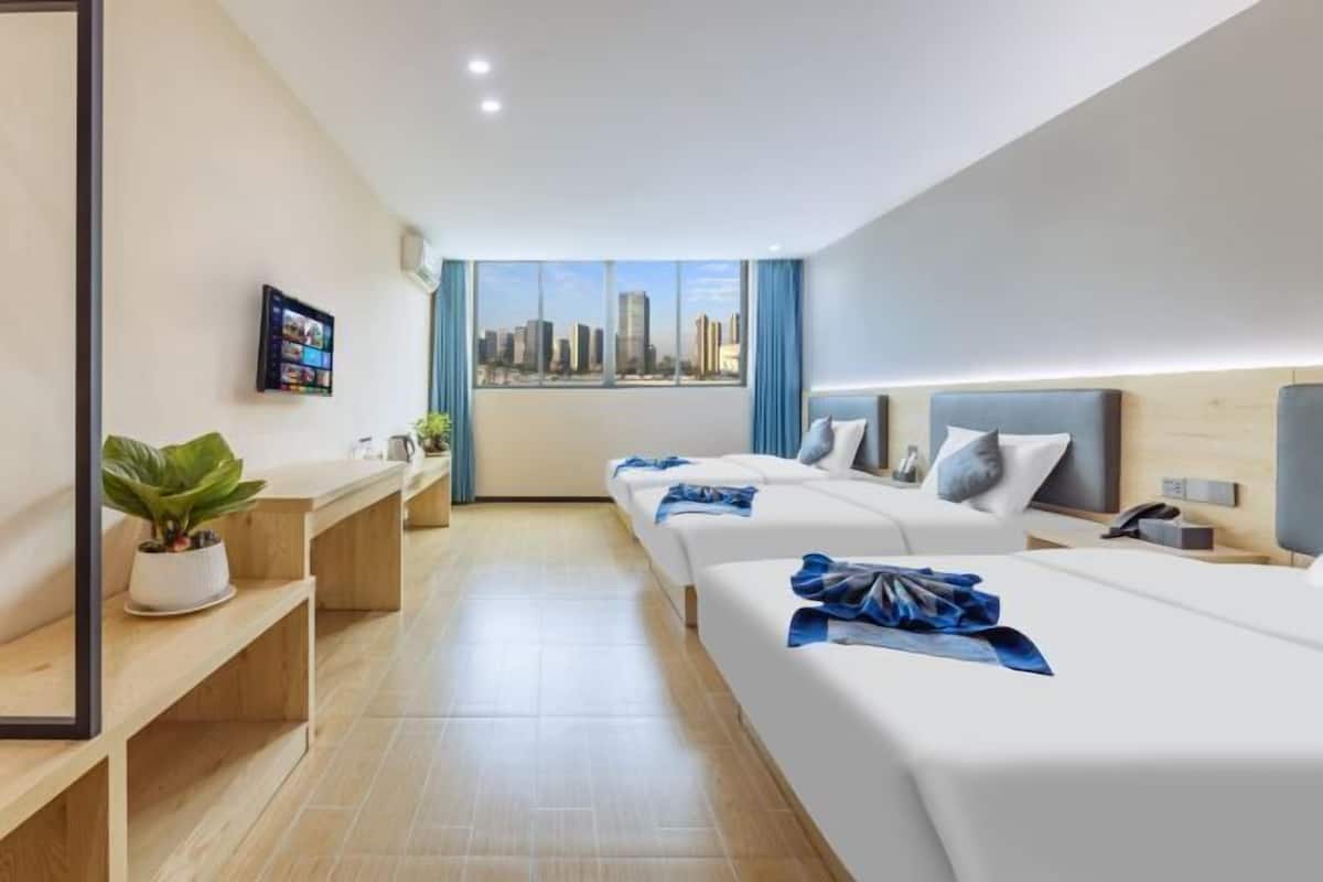 A hotel room with a city view, two beds, a desk, a plant, and a TV on the wall.