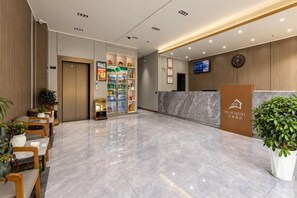 Een hotel receptie met een marmeren vloer, een receptiebalie, een klok en een televisiescherm.
