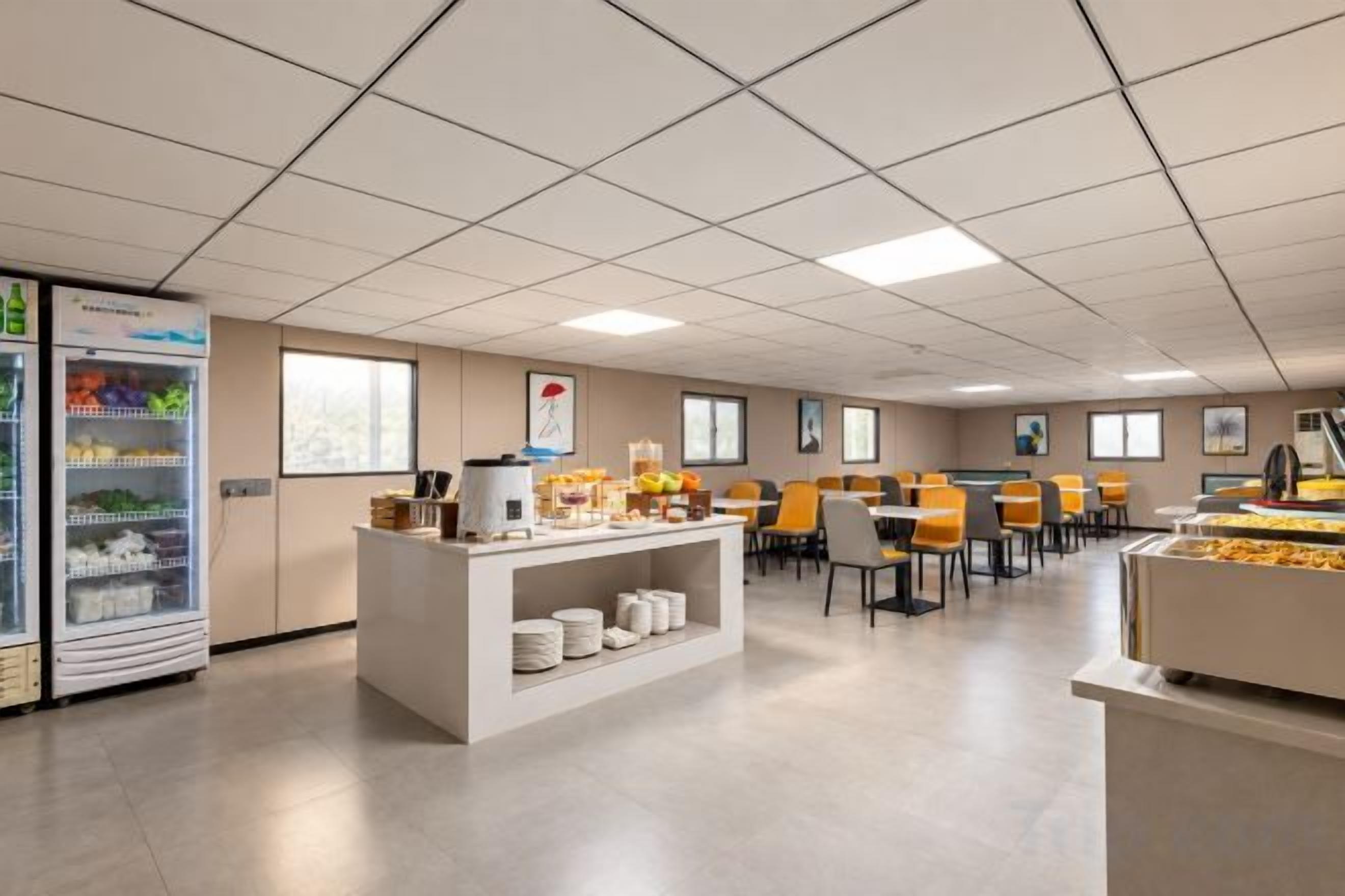 Un espace de restauration d’hôtel avec un buffet, un réfrigérateur rempli de boissons et plusieurs chaises.