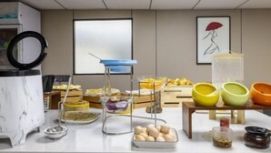 A buffet setup with various dishes and utensils on a table, a marble kitchen island, and a large window in the background. - Heyi Express Hotel (Zhuhai Baijiao Science Park Doumen Bus Terminal) (Zhuhai)