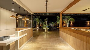 Un interior moderno con mostrador de recepción, paneles de madera, iluminación colgante y un arreglo de plantas central.