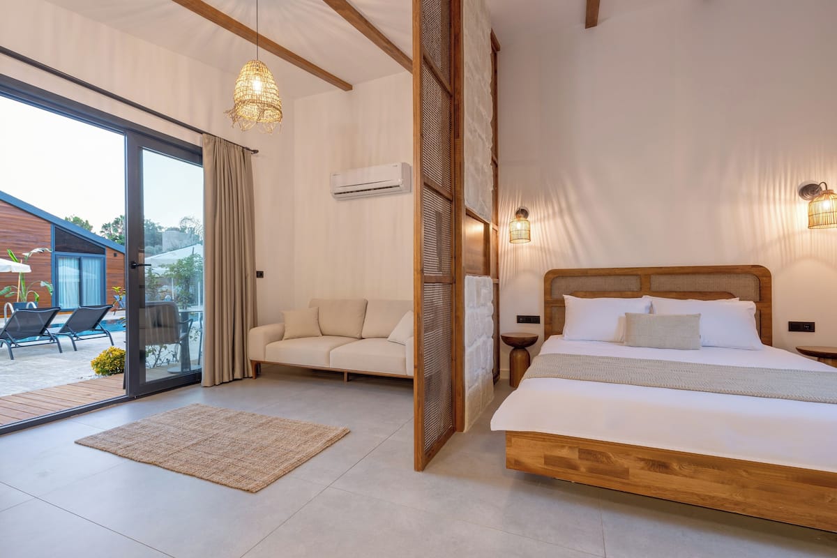 A modern bedroom with a large bed, a sofa, a glass door leading to a balcony, and a ceiling fan.