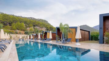 Relax by the pool surrounded by lush greenery and hills, with lounge chairs and umbrellas at your disposal.