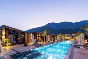 A modern pool area with lounge chairs and umbrellas, wooden buildings, and a mountain backdrop. - Rota Kilidonia Karaöz Suites&Villas (Kumluca)