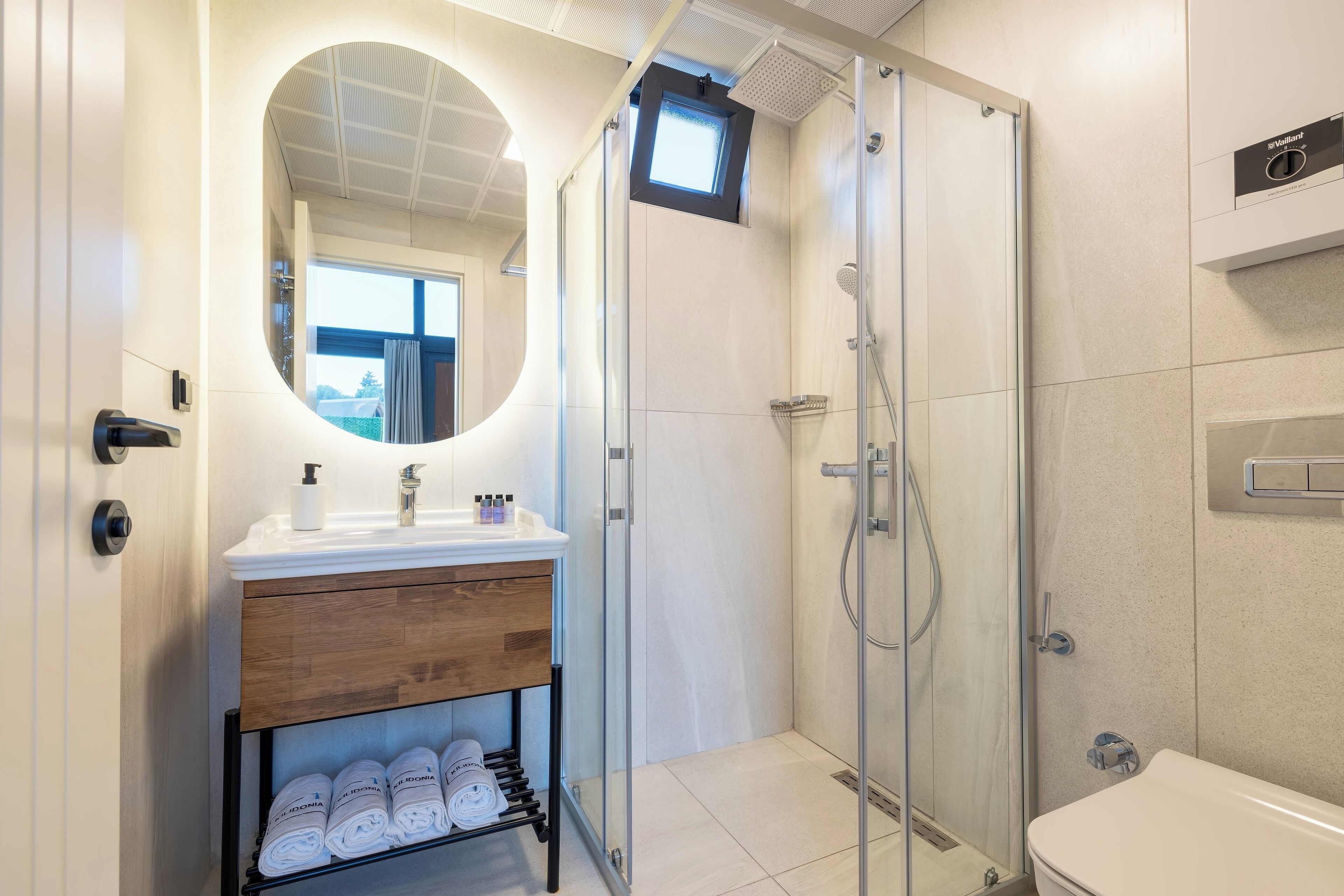 A modern bathroom with a glass-enclosed shower, a wooden vanity with a mirror, and neatly folded towels on a rack.