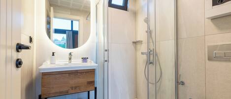 A modern bathroom with a glass-enclosed shower, a wooden vanity with a mirror, and neatly folded towels on a rack.