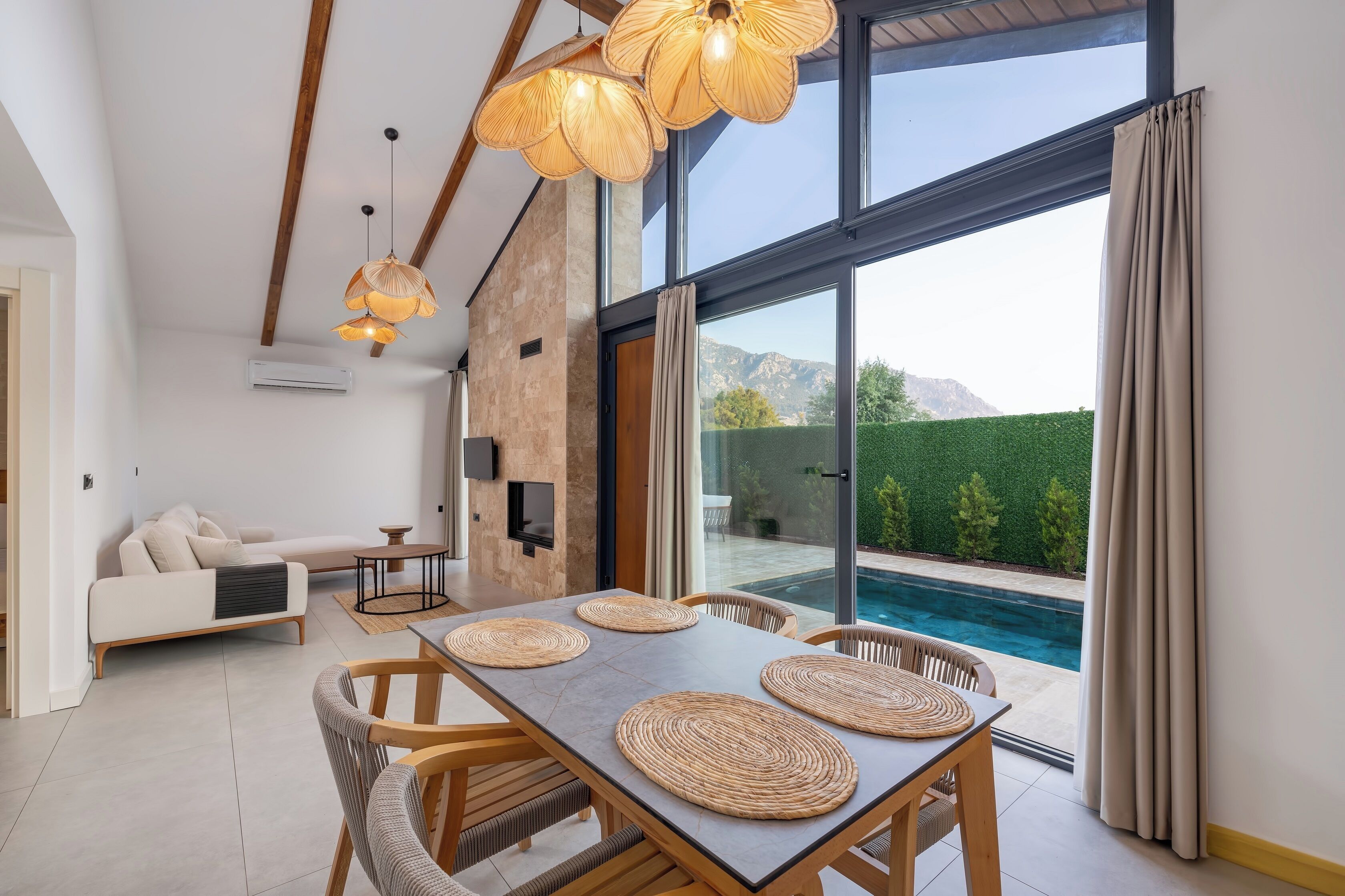 A modern living room with a dining area, large windows, and a view of a swimming pool.