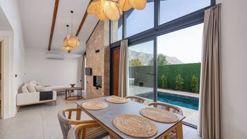 A modern living room with a dining area, large windows, and a view of a swimming pool.