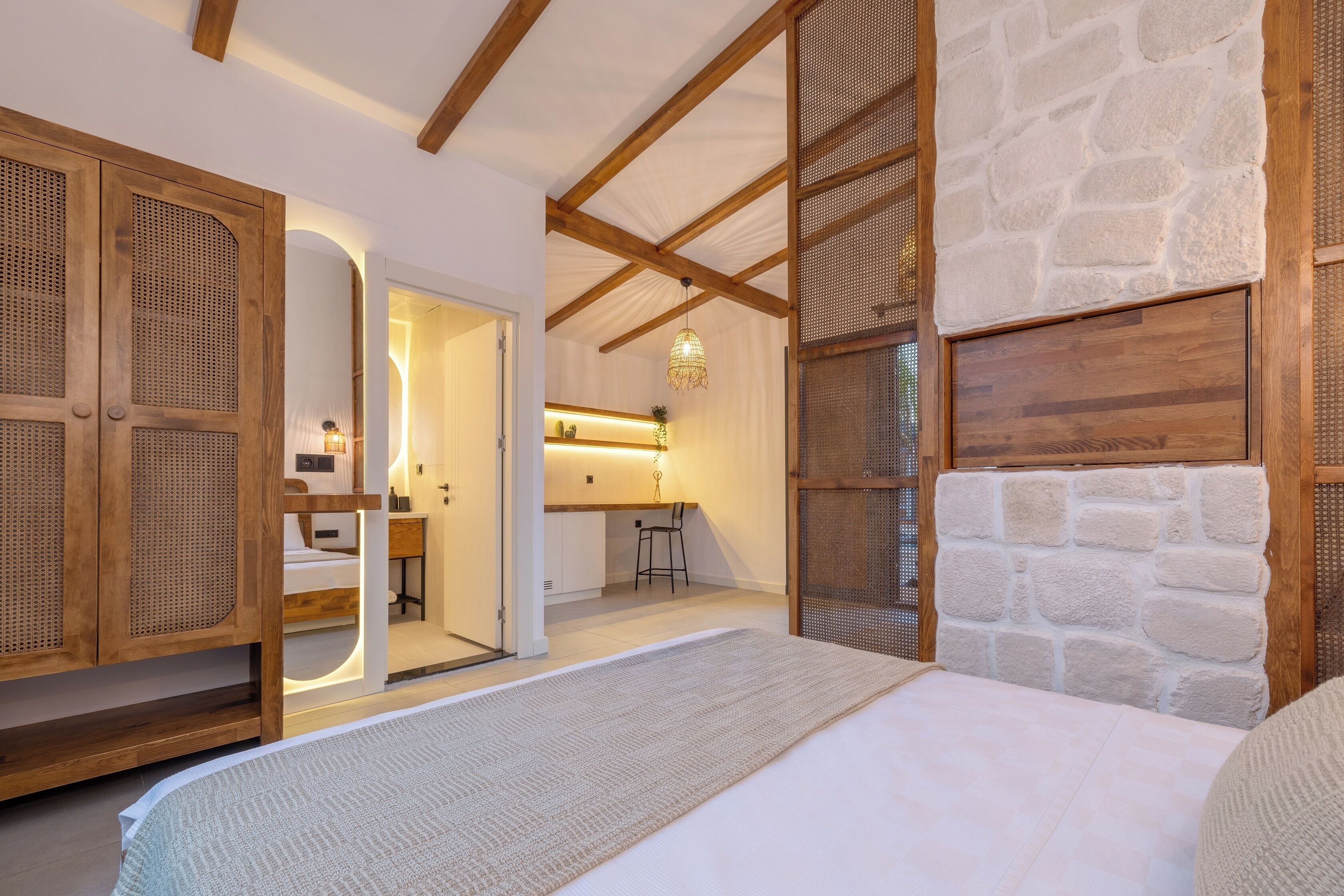 Une chambre avec un lit, une armoire en bois, un mur en pierre et, au fond, une petite kitchenette.