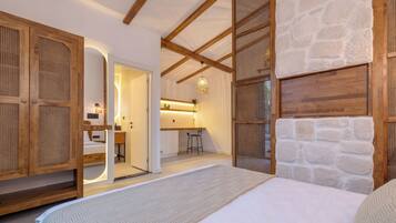 Une chambre avec un lit, une armoire en bois, un mur en pierre et, au fond, une petite kitchenette.
