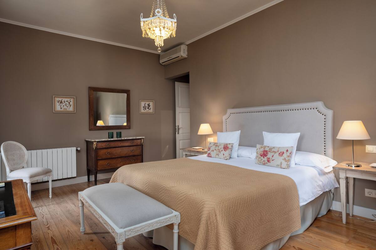 Une chambre à coucher avec un grand lit, deux tables de chevet avec des lampes, une commode, une chaise et un lustre.