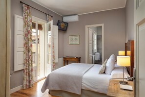 Une chambre à coucher avec un lit, une table de chevet avec une lampe, un téléviseur fixé au mur et une fenêtre avec des rideaux.