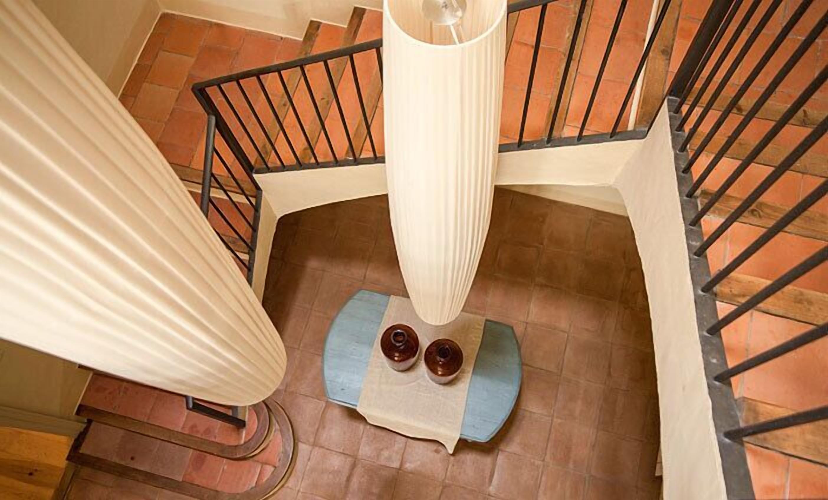 Un escalier en colimaçon avec une main courante, un tapis bleu au bas et deux petits récipients posés sur le tapis.