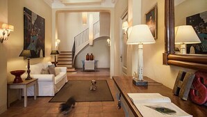 Un salon spacieux avec un escalier, un canapé blanc, une table basse et un chien qui joue sur un tapis.