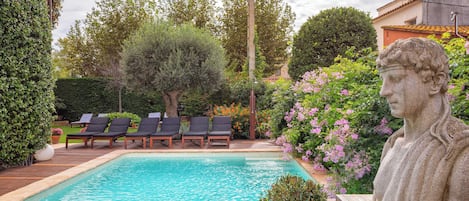 A swimming pool with lounge chairs, surrounded by greenery and a stone bust.