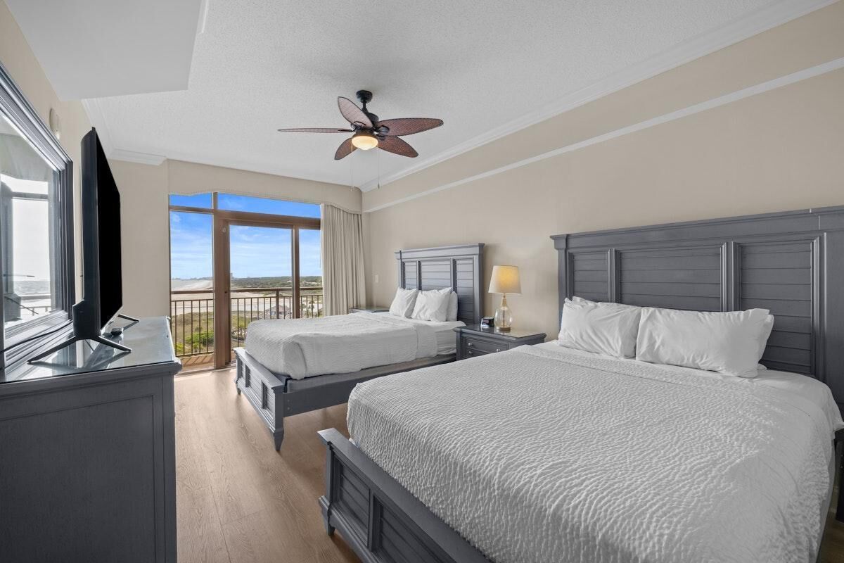 Une chambre d’hôtel avec deux lits, un ventilateur de plafond, une télévision et un balcon avec vue.