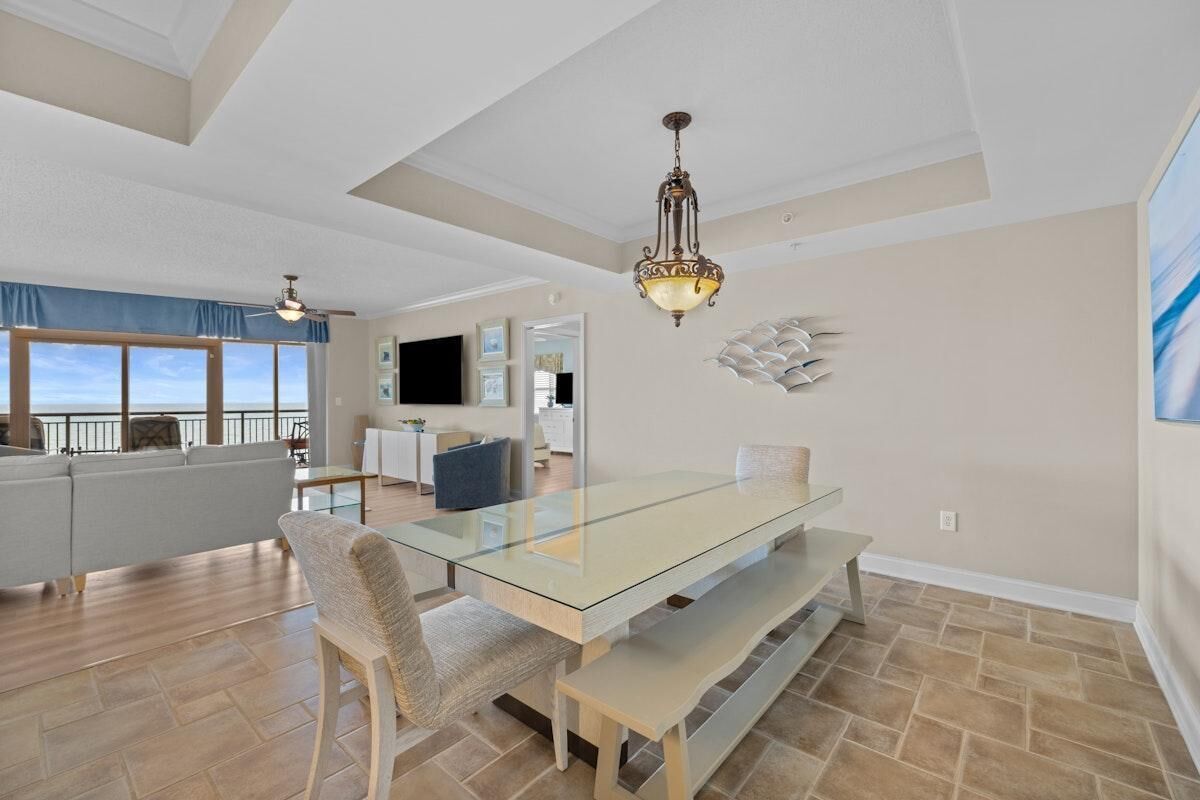 A spacious living area with a glass-top dining table, a sofa, and a television.