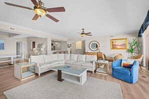 A living room with a sectional sofa, a coffee table, a blue armchair, two side tables, and ceiling fans. - Dream Come True: 5 Bdrm Oceanfront Condo (North Myrtle Beach)