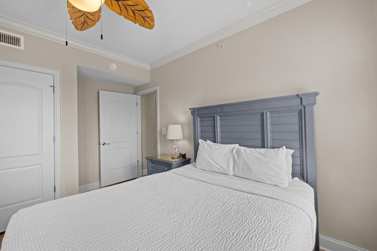 Un dormitorio con una cama grande, una mesita de noche con lámpara y un ventilador de techo con luces en forma de hojas.