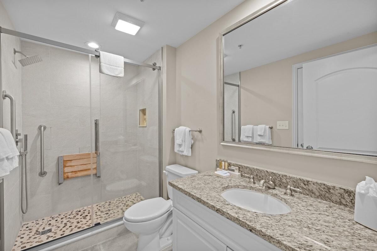 A modern bathroom with a glass shower enclosure, a toilet, a sink with a marble countertop, and a large mirror.