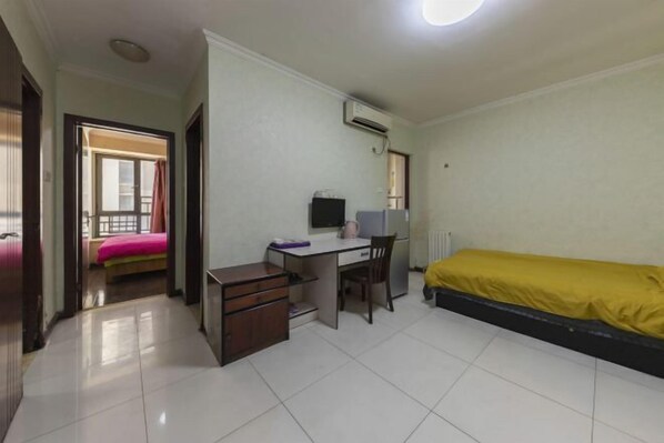 A small, clean room with a bed, a desk, and a chair. There is a window with curtains, an air conditioning unit, and a door leading to another room. - Zhengzhou Ruxinjia Apartment (Zhenghong Digital Apartment) (Zhengzhou)