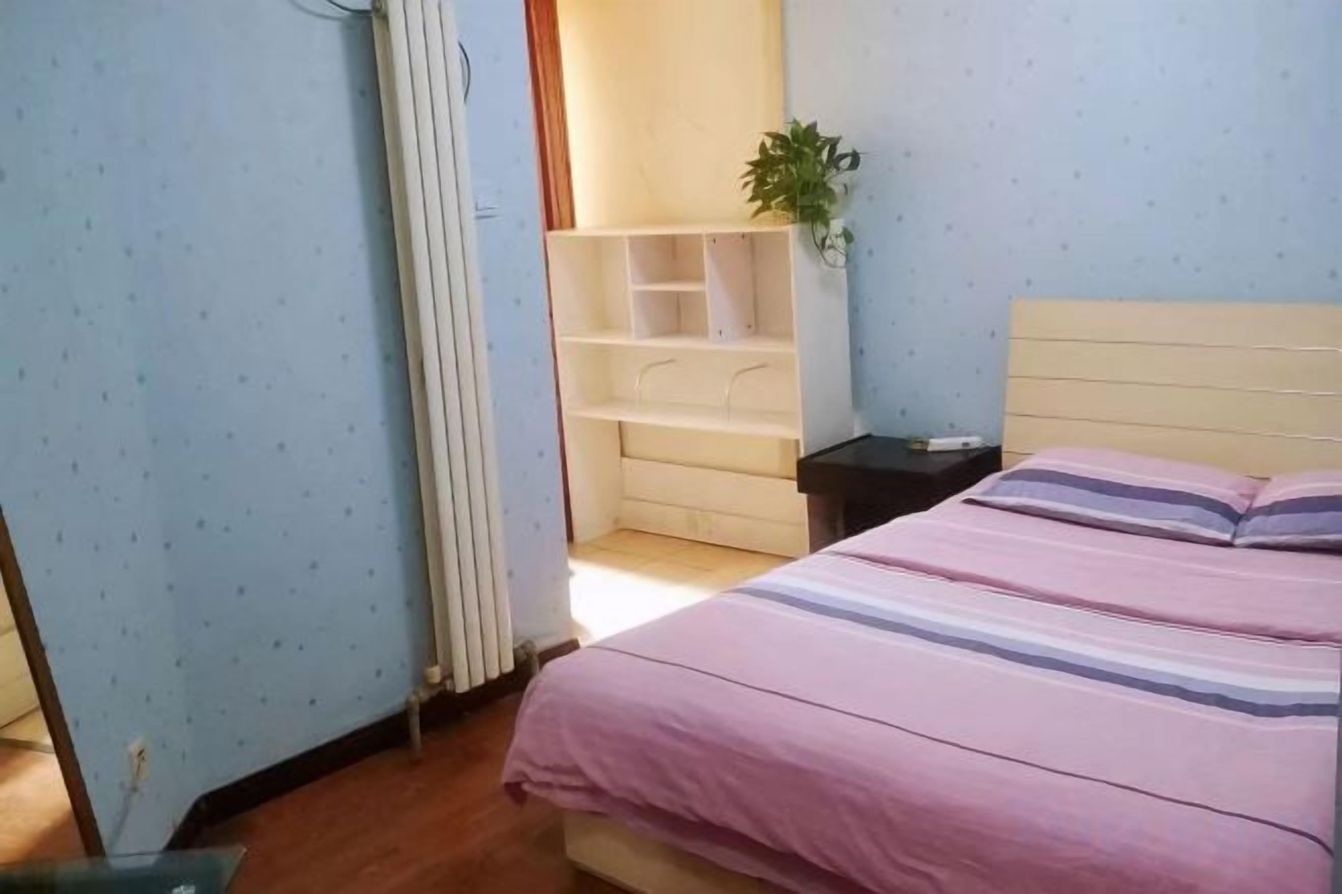 A bedroom with a bed, a nightstand, a radiator, and a plant.