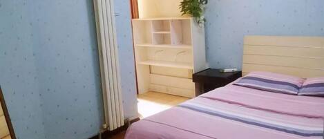 A bedroom with a bed, a nightstand, a radiator, and a plant.