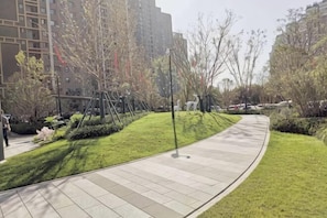 A landscaped pathway with grass and trees, surrounded by buildings. - Zhengzhou Ruxinjia Apartment (Zhenghong Digital Apartment) (Zhengzhou)
