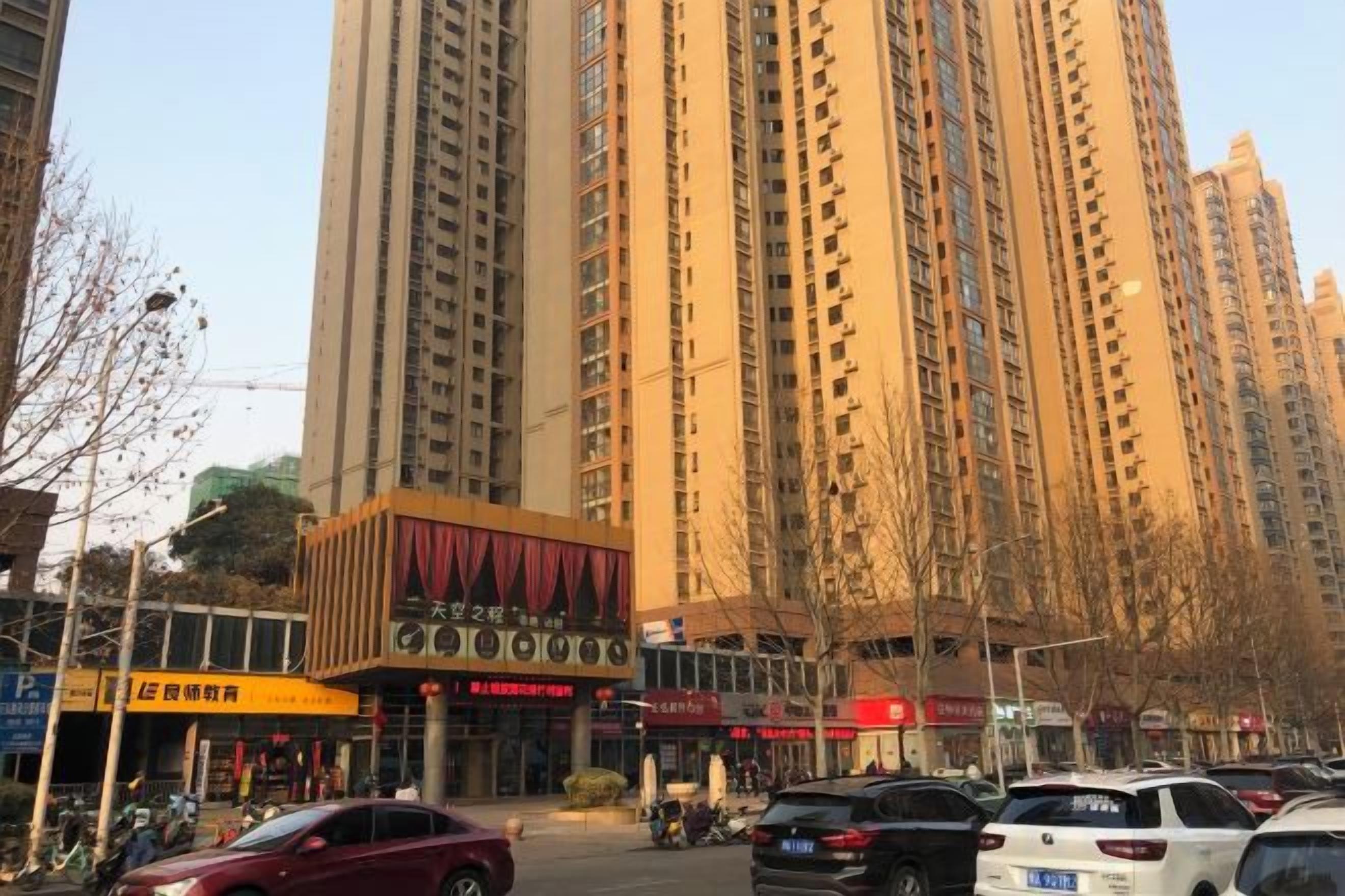 A high-rise building with multiple floors, a commercial area with shops, and parked cars.