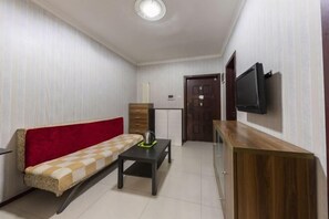 A small, furnished room with a sofa, a coffee table, a TV mounted on the wall, and a wooden cabinet. - Zhengzhou Ruxinjia Apartment (Zhenghong Digital Apartment) (Zhengzhou)