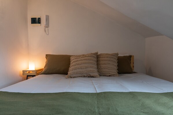 A bedroom with a bed, pillows, a bedside table with a lamp, and a wall-mounted phone.