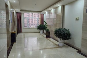 Pasillo de hotel con vistas a edificios, plantas en macetas y suelo de baldosas.
