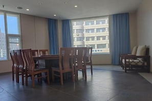 Una habitación con una mesa de comedor y sillas, un sofá, ventanas grandes con cortinas y vistas a edificios.