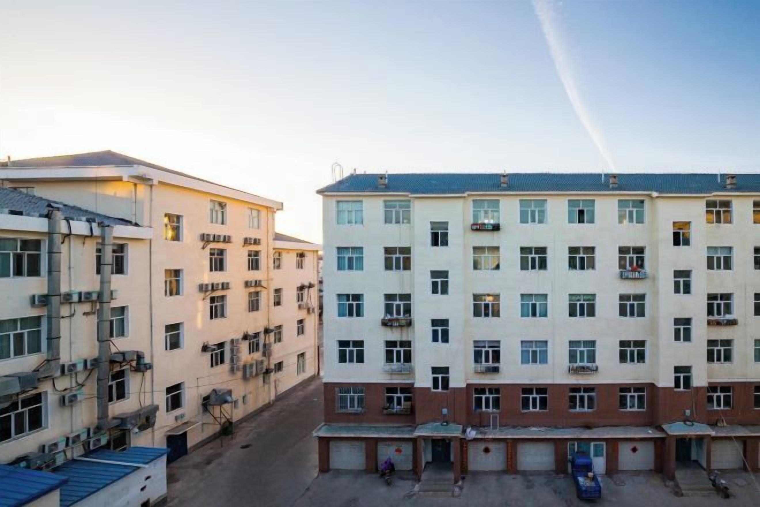 A multi-story building with a central courtyard, multiple balconies, and a parking area.