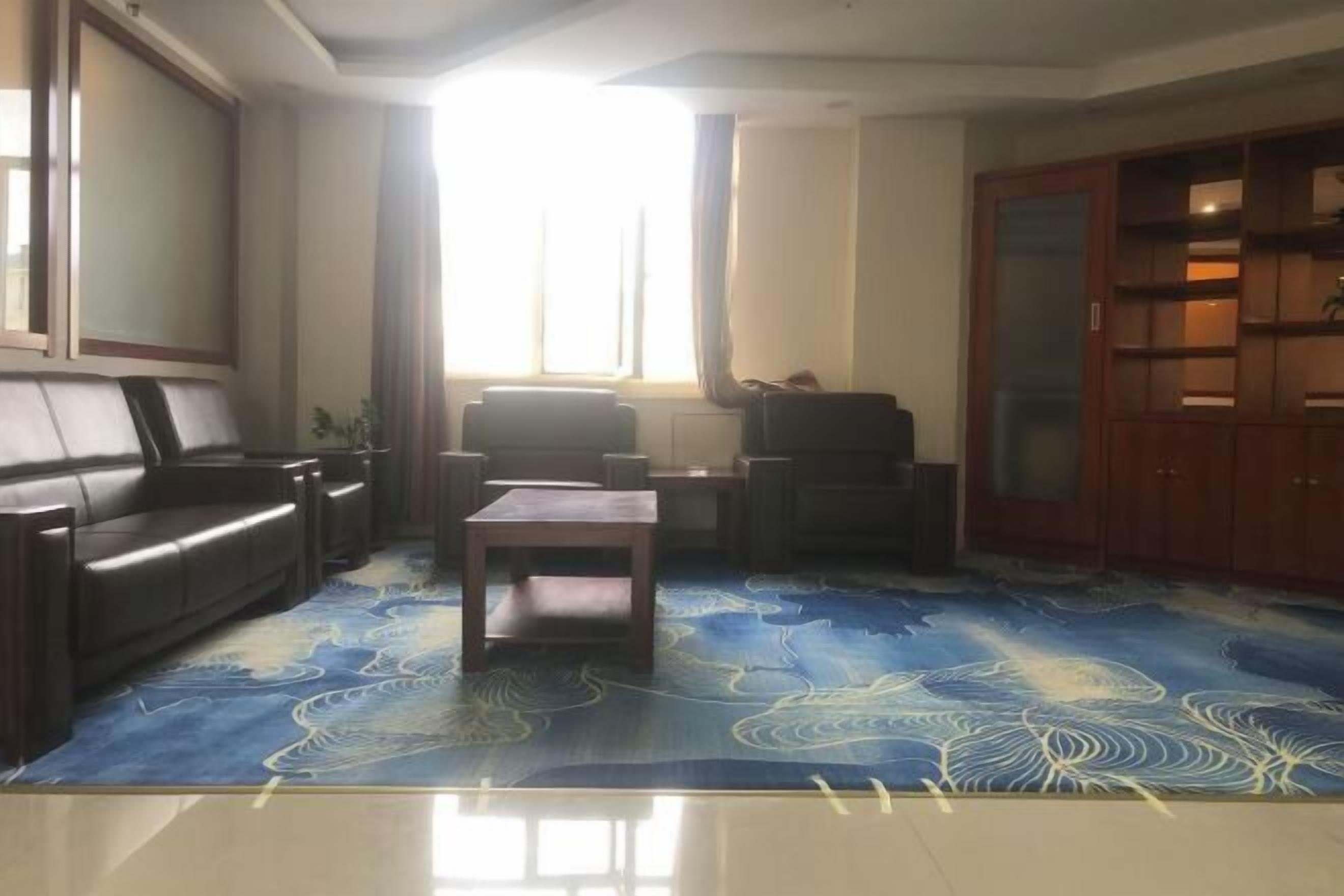 Ein Wohnzimmer mit Sofa, Couchtisch und Fernseher. Ein Fenster mit Vorhängen und ein Schrank mit Glastüren.