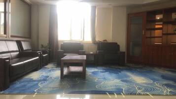 A living room with a sofa, a coffee table, and a TV. There is a window with curtains, and a cabinet with glass doors.