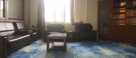 Ein Wohnzimmer mit Sofa, Couchtisch und Fernseher. Ein Fenster mit Vorhängen und ein Schrank mit Glastüren.
